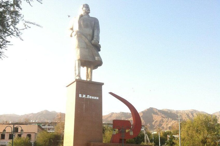 A statue of a seated figure on a pedestal with a name inscription, set against a mountainous backdrop. 3