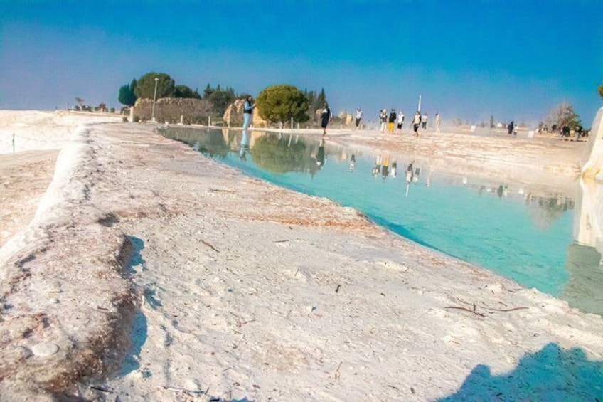 A salt flat with a reflective pool, a clear sky, and distant trees. 5