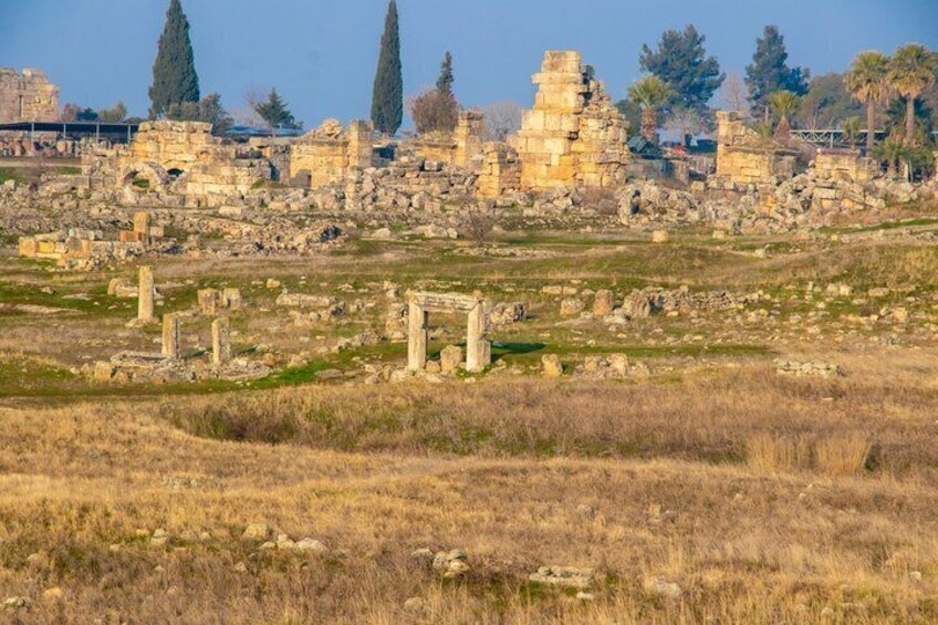 Ancient ruins with stone columns and structures in a grassy field. 3