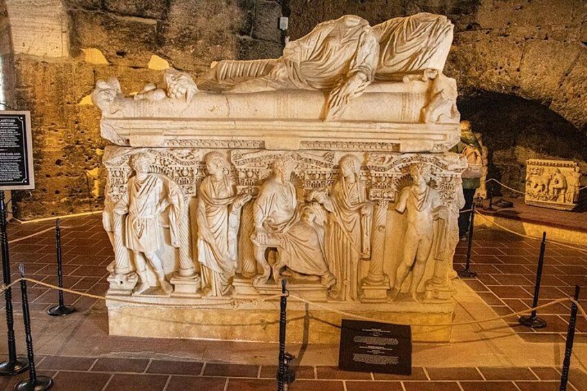 A marble sarcophagus with relief sculptures depicting figures in ancient attire, surrounded by a protective barrier. 3
