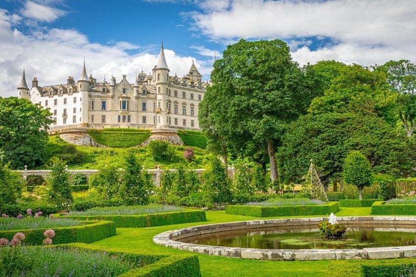 A large, ornate castle surrounded by lush gardens and a pond. 1