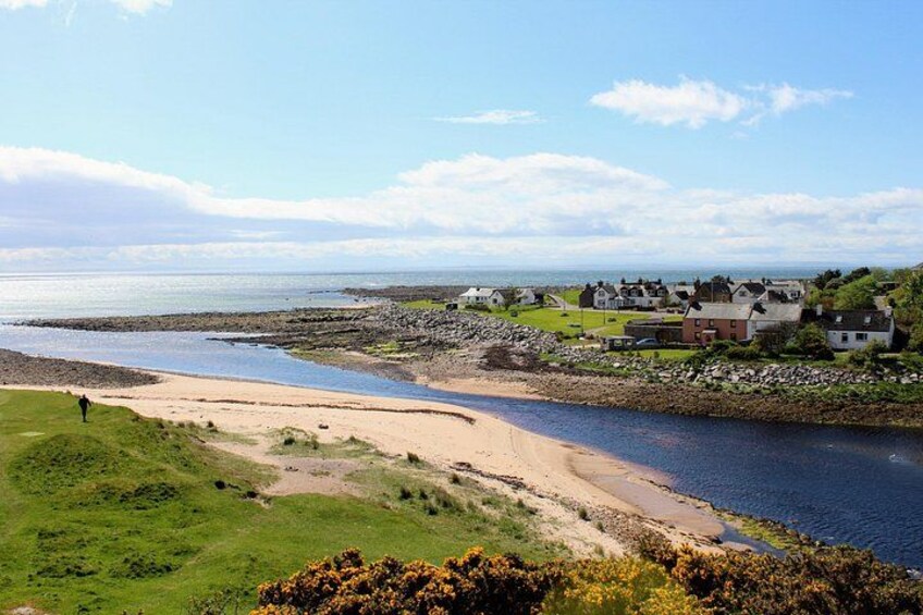 A coastal landscape with a sandy beach, a rocky shoreline, and houses in the background. 3