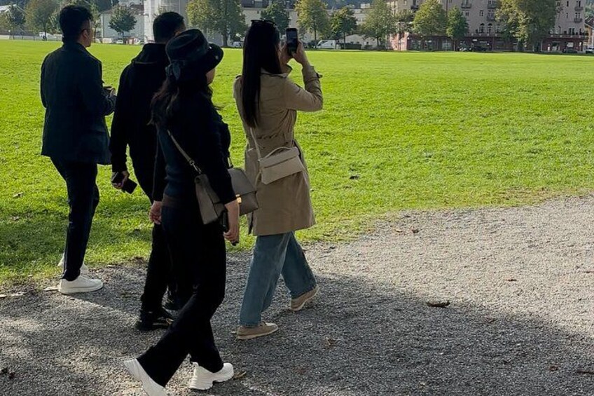 A group of people walking in a park with a grassy field and a building in the background. 5