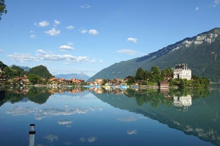 A calm lake with a reflection of buildings and mountains, a clear sky, and a distant mountain peak. 2