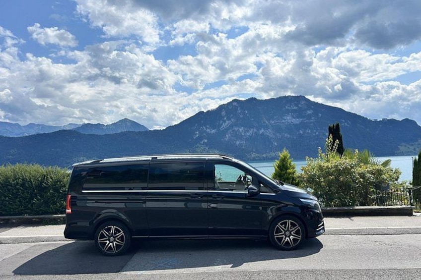 Un furgone nero parcheggiato su una strada, con uno sfondo di montagne e un lago. 2