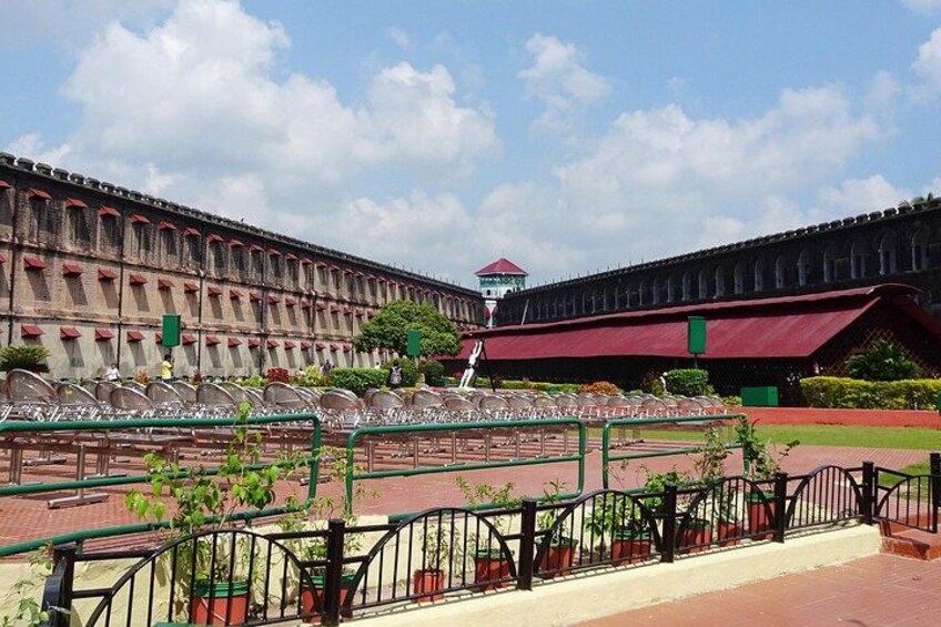 A courtyard with a large building, a red-roofed structure, and a green fence. 3