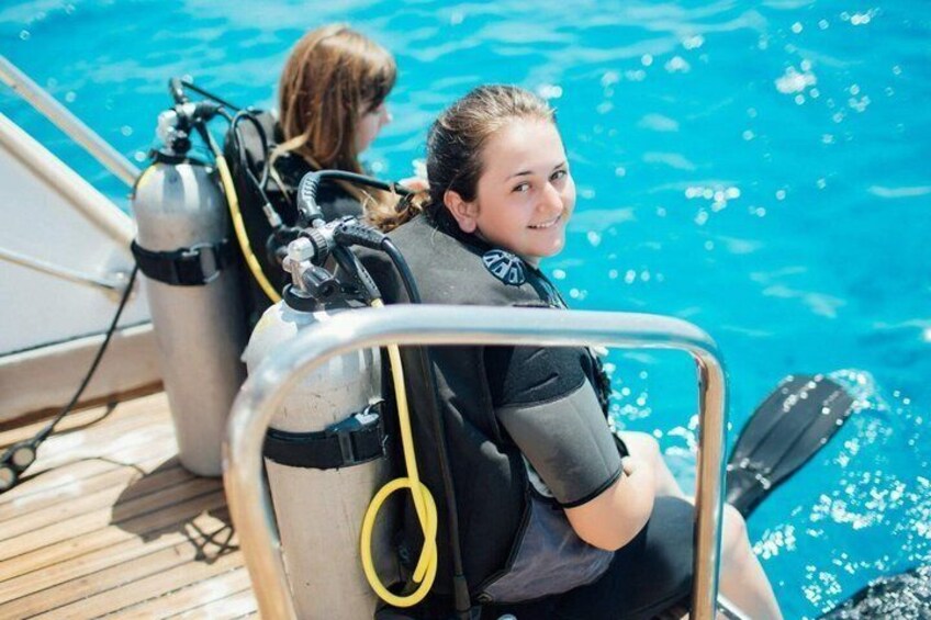 Two people in scuba diving gear seated by a pool. 3