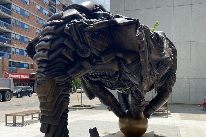 A large metallic sculpture of a horse in motion, positioned on a paved area with a building and a truck in the background. 4