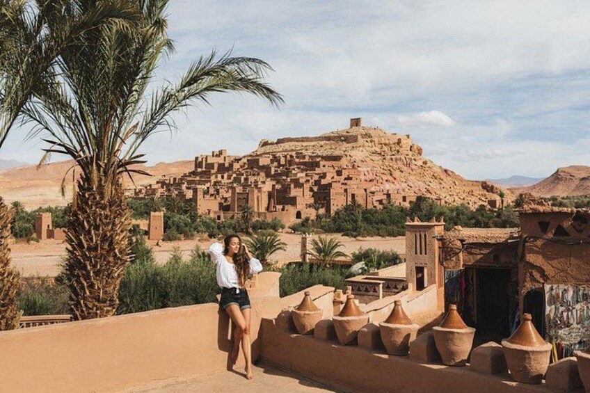 A person standing on a rooftop overlooking a traditional village with terracotta pots and palm trees. 5