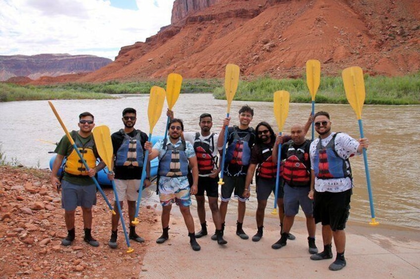 A group of people standing by a river, holding paddles, wearing life jackets, and standing on a concrete ledge. 4
