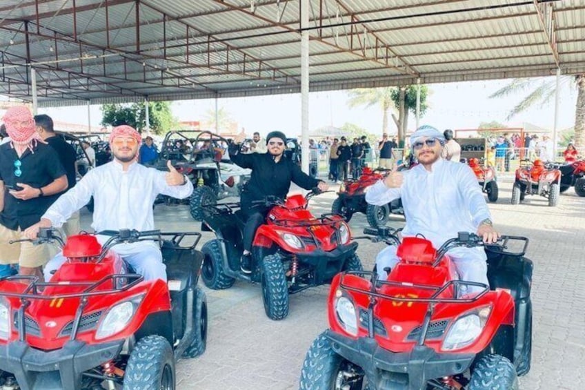 Three individuals on red quad bikes, a covered area, and a crowd in the background. 4