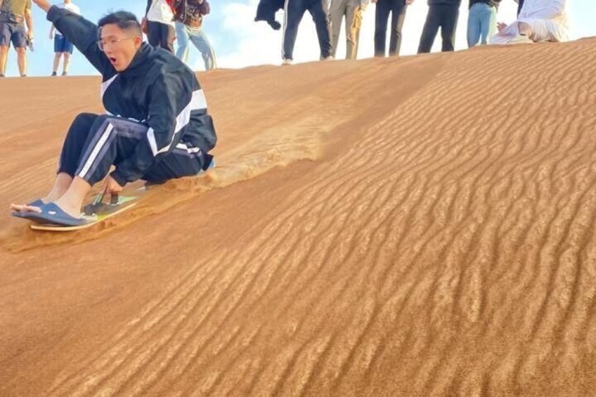 A person sliding down a sandy slope with others watching. 2