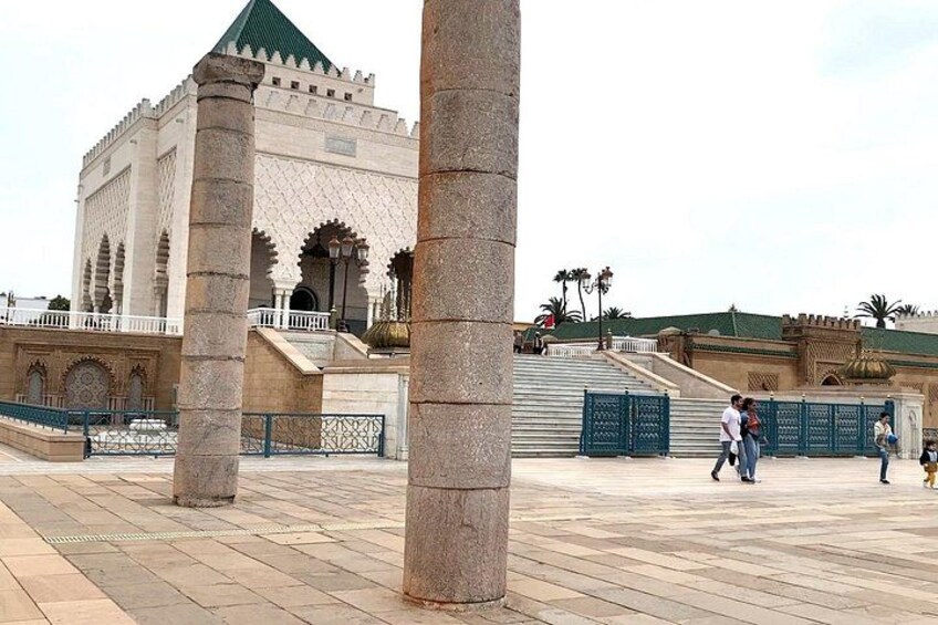A historical building with arches and columns, a paved plaza, and people walking. 2