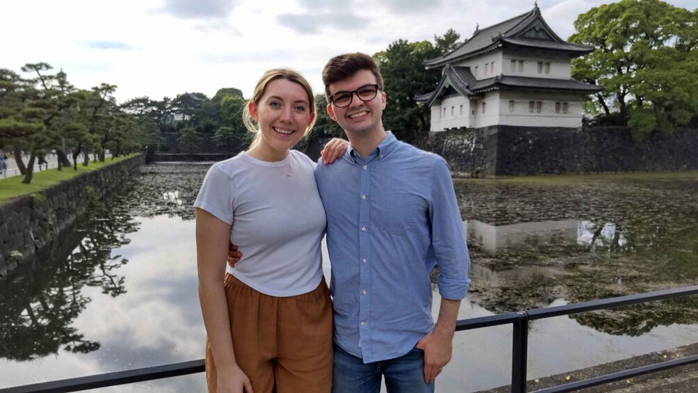 Two people standing by a calm body of water with a traditional Japanese castle in the background. 5