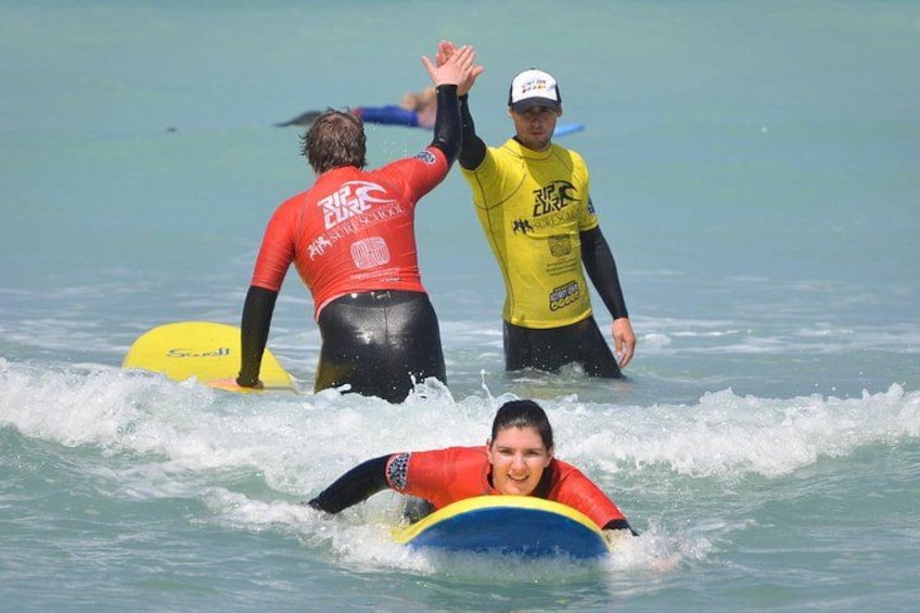 Three people in the ocean, one on a surfboard and two in wetsuits. 1