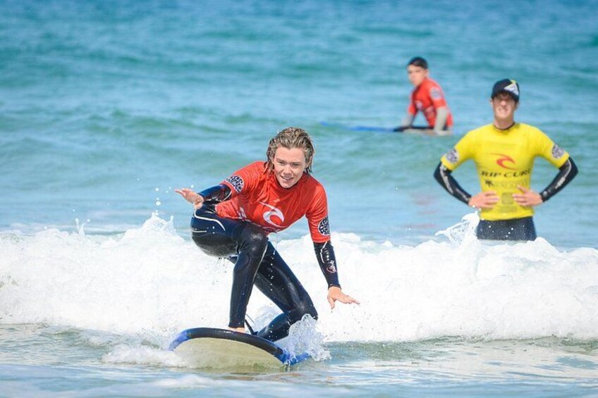 A person surfing on a wave, another person in the background, and a third person in a yellow shirt. 1