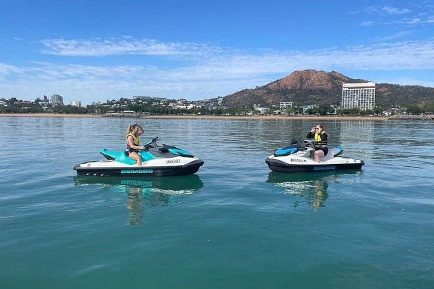 Deux jet-skis sur une étendue d’eau calme, avec une montagne et des bâtiments en arrière-plan. 4