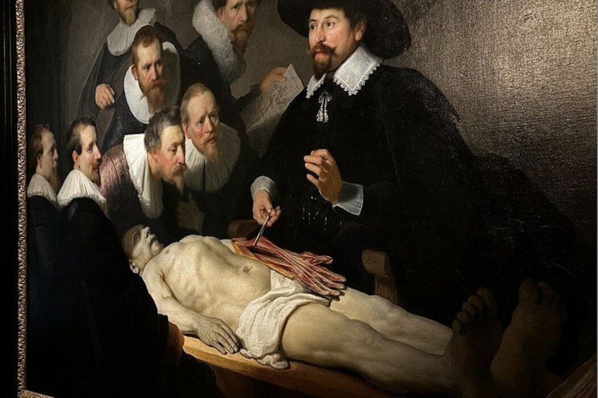 En historisk scene med en gruppe mennesker samlet omkring en person, der ligger på et bord, muligvis en medicinsk demonstration eller obduktion. 5