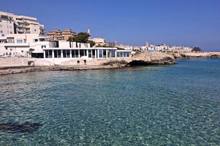 A coastal town with clear blue waters, a white building with a glass facade, and rocky cliffs. 3