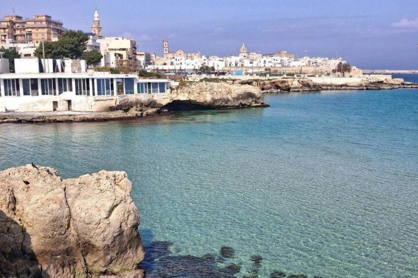 A coastal town with clear blue waters, rocky coastline, and white buildings. 4