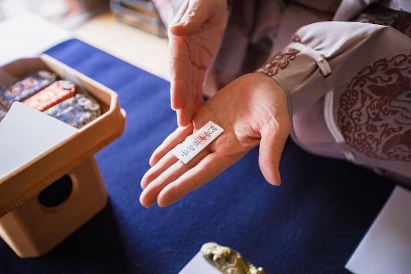 A person holding a card with text, a wooden box with items, and a blue cloth. 3