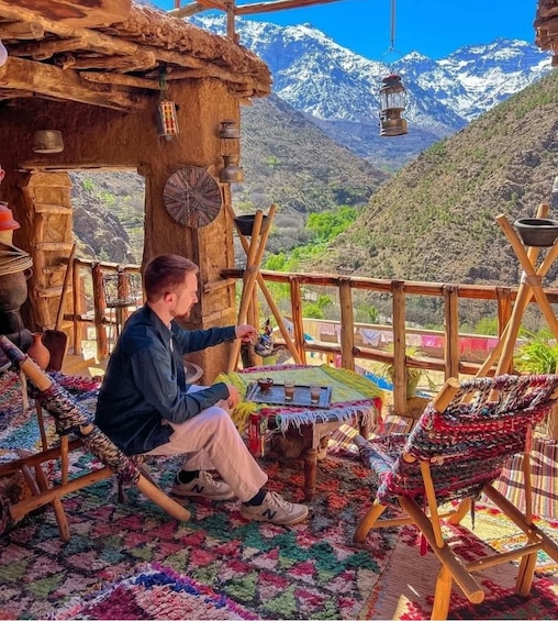 A person painting in a rustic outdoor setting with colorful rugs and traditional furniture, overlooking a mountainous landscape. 5
