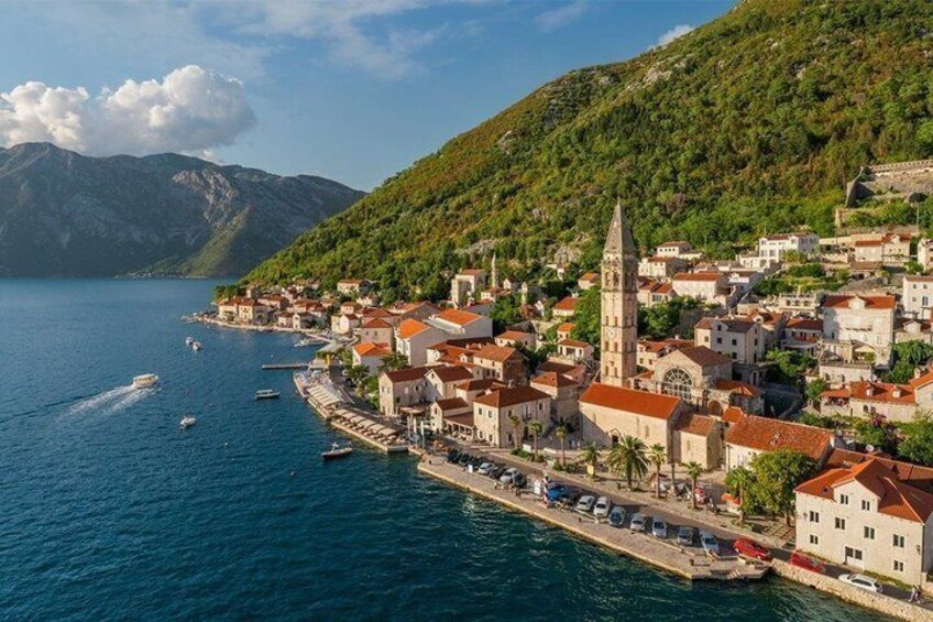 A coastal town with a prominent church, boats on the water, and a mountainous backdrop. 5