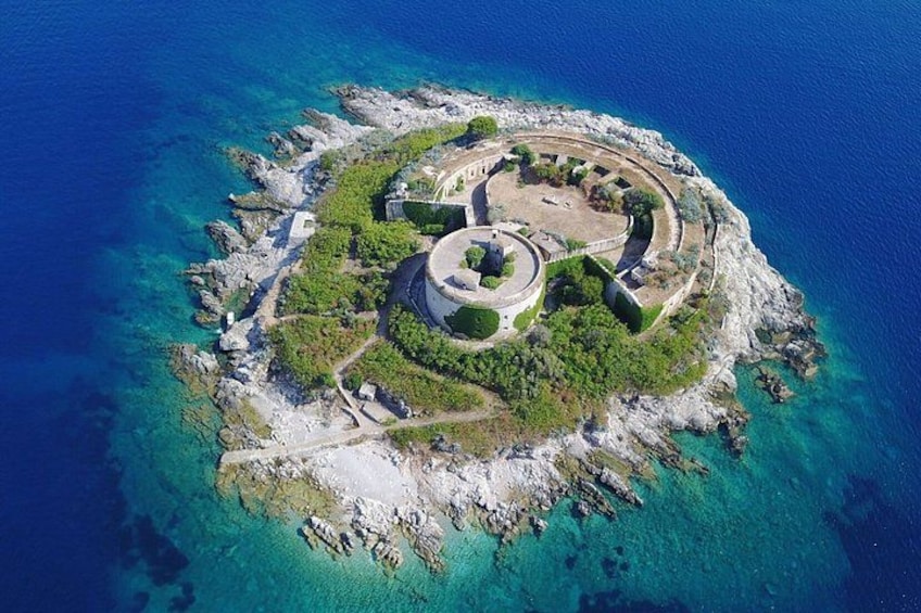 An aerial view of a circular island with a central structure surrounded by greenery and rocky terrain. 1