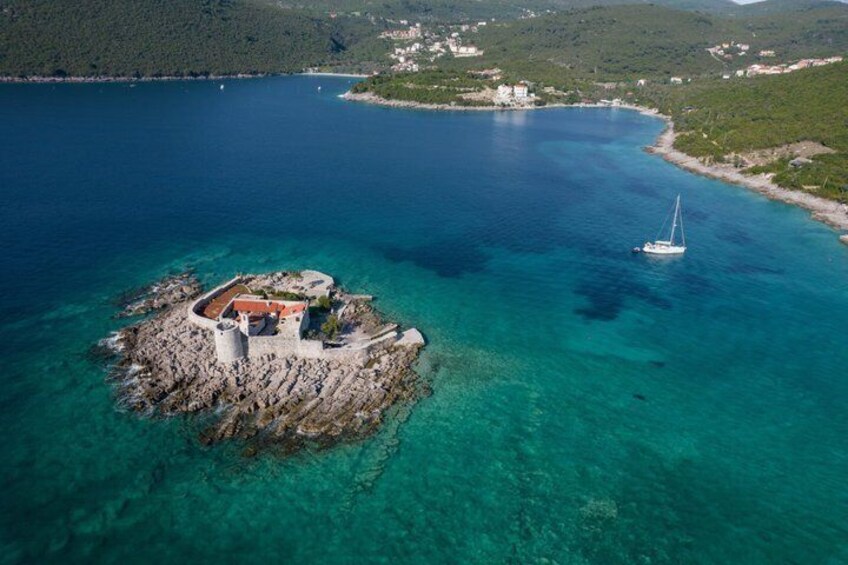 An aerial view of a rocky island with a lighthouse and a sailboat in the water. 3