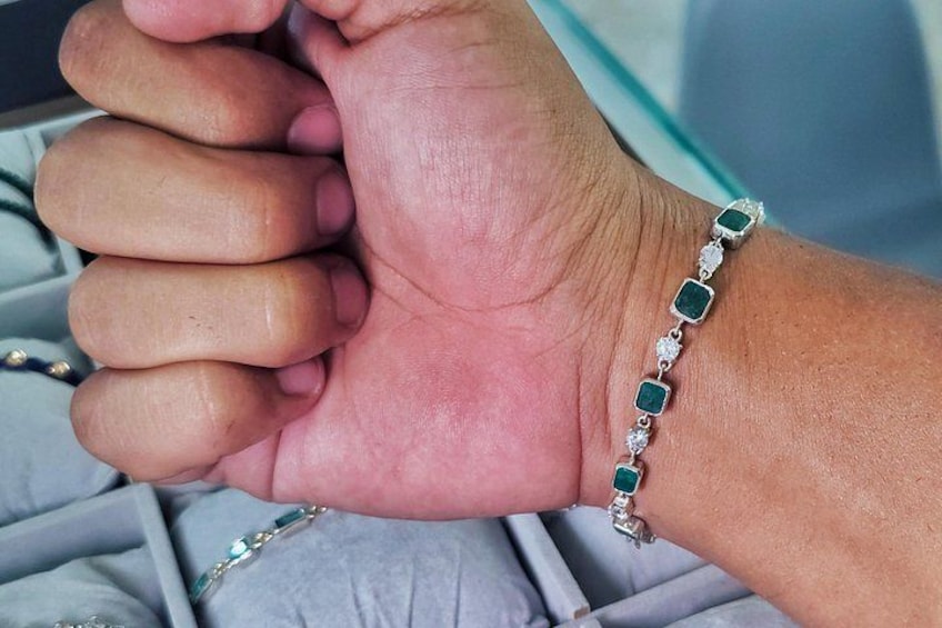 En hånd med et armbånd med grønne sten og diamanter. 5