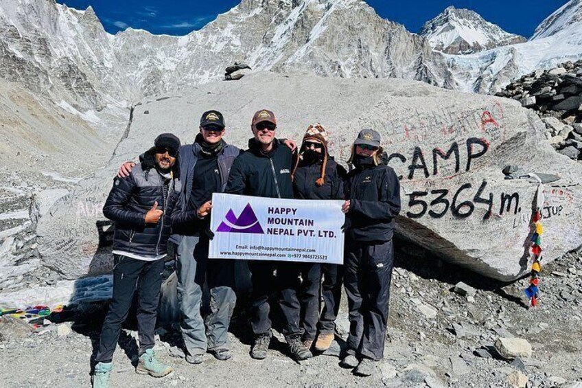 Un groupe de personnes se tient devant un rocher sur lequel est inscrit « CAMP 5364 m ». 2