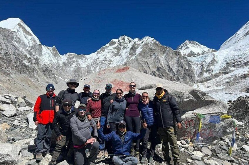 Un groupe de personnes posant sur le sommet rocheux d’une montagne, avec des montagnes enneigées en arrière-plan. 1