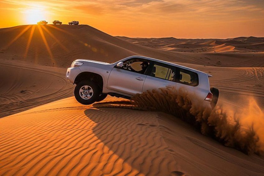 A white SUV driving through a desert with sand dunes and a sunset in the background. 3