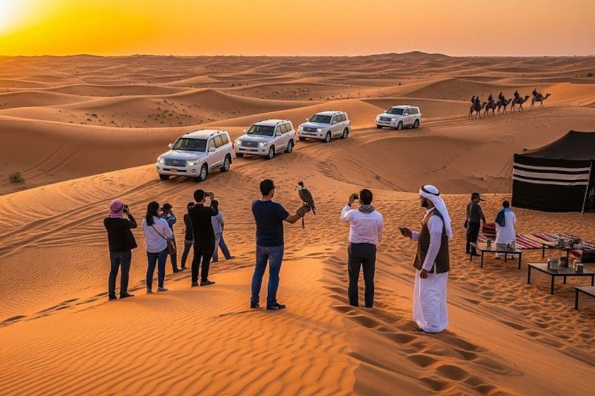 A desert landscape with sand dunes, a group of people observing, and several white vehicles. 1
