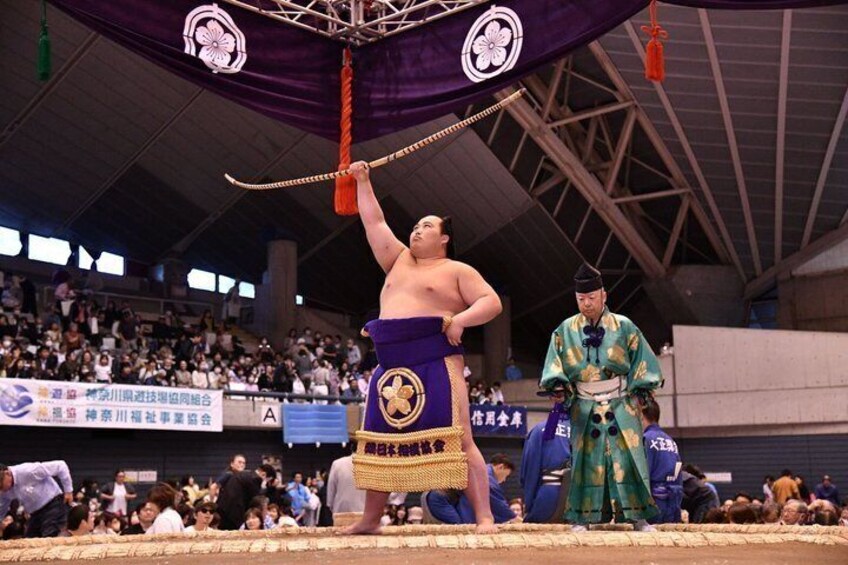 A sumo wrestler performing a ritual with a rope in a stadium. 2