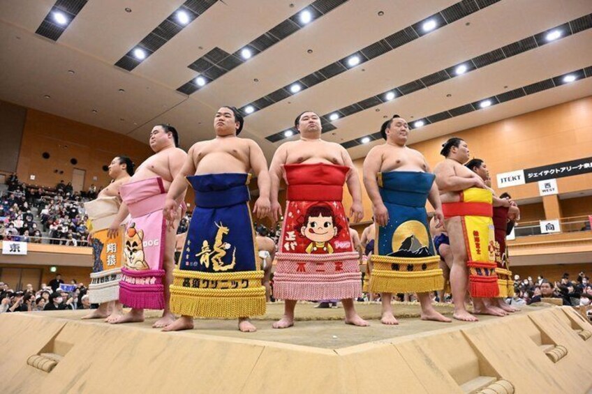 Sumo wrestlers standing on a platform with spectators in the background. 1