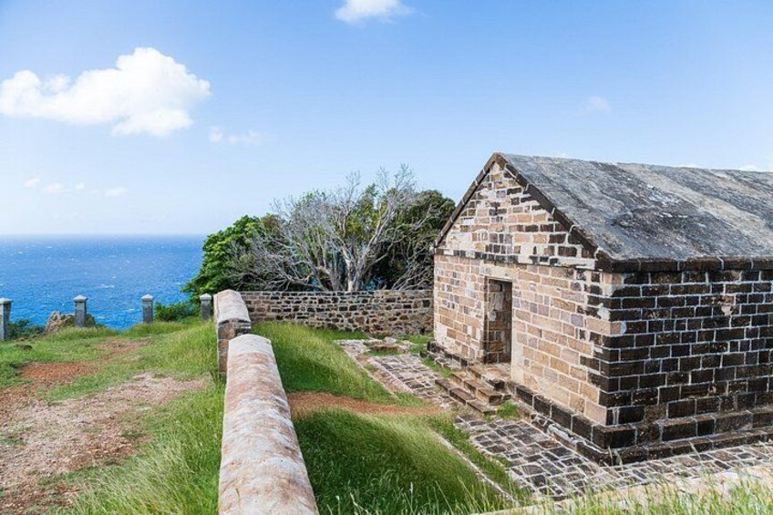 Un edificio de ladrillo con una pared de piedra, un cañón y vista al océano. 3