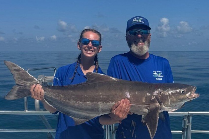 Two people holding a large fish on a boat with the ocean in the background. 2