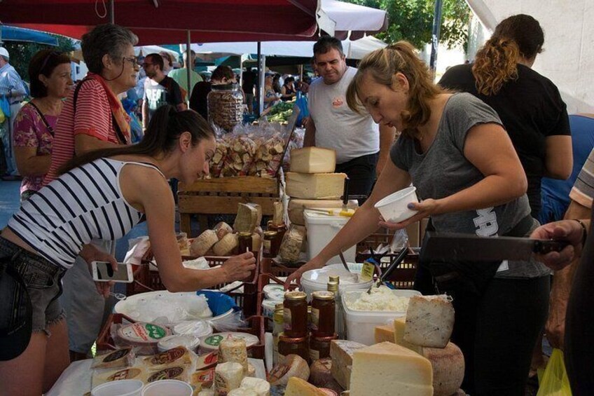 People at a market stall with various cheeses and food items. 4