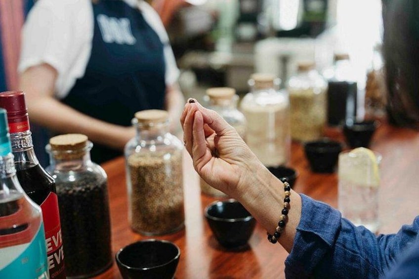 A person holding a small object, possibly a spice or seasoning, with various bottles and containers of spices and condiments on a table. 1