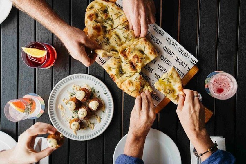 A group of people sharing a meal with pizza and drinks on a wooden table. 4