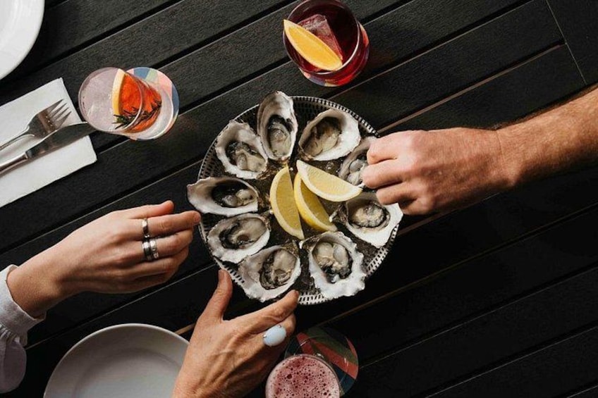 A top-down view of a dining table with a plate of oysters, lemon wedges, and two cocktails. 5