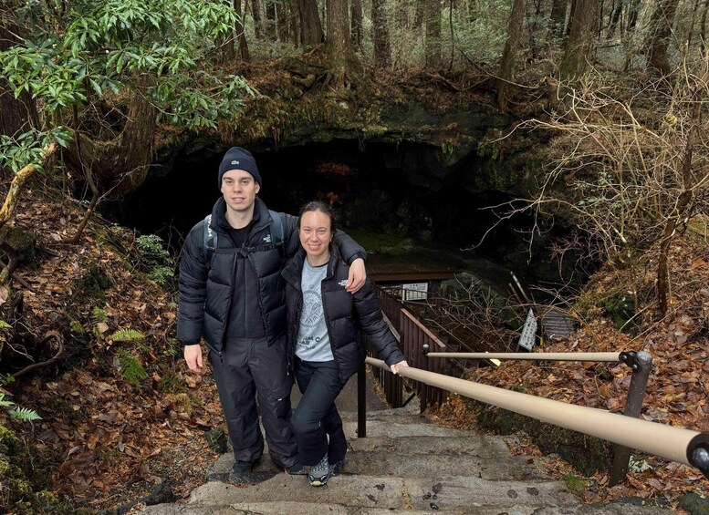 Two people walking on a stone staircase in a forested area with a wooden railing and a sign in the background. 1