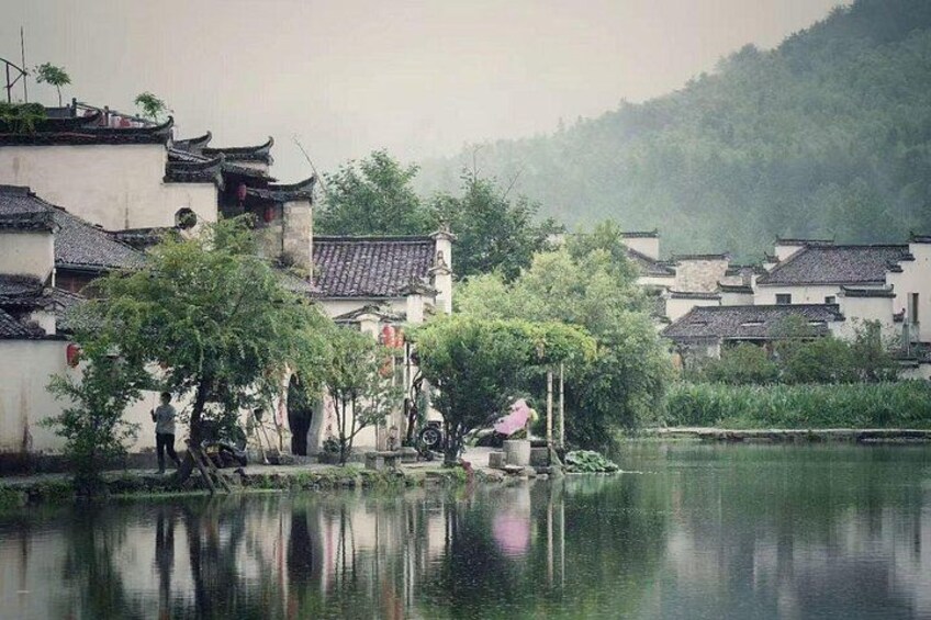 A traditional Chinese village with buildings, a calm river, and a misty mountain in the background. 4