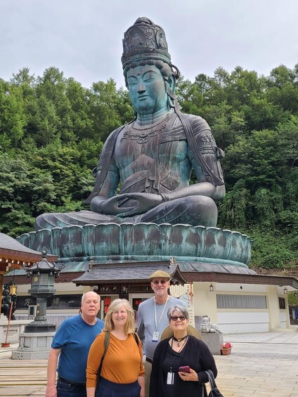 A large seated Buddha statue with intricate carvings, surrounded by lush greenery and traditional architecture. 5