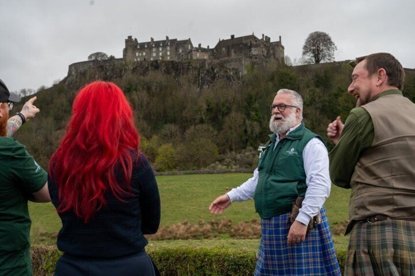 Un grupo de personas de pie al aire libre con un castillo en el fondo. 2