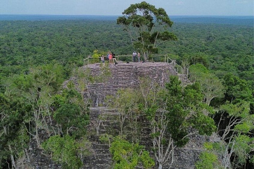 Ein Steingebäude, auf dem sich Personen befinden, umgeben von dichtem Wald. 4