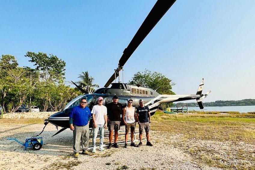 Ein Hubschrauber, der auf einer unbefestigten Fläche geparkt ist, mit einem Gewässer und Palmen im Hintergrund. 5