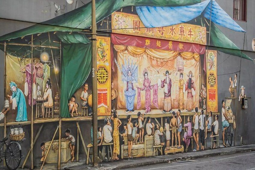 A mural with traditional figures and a stage, set up on a street with a green canopy. 2
