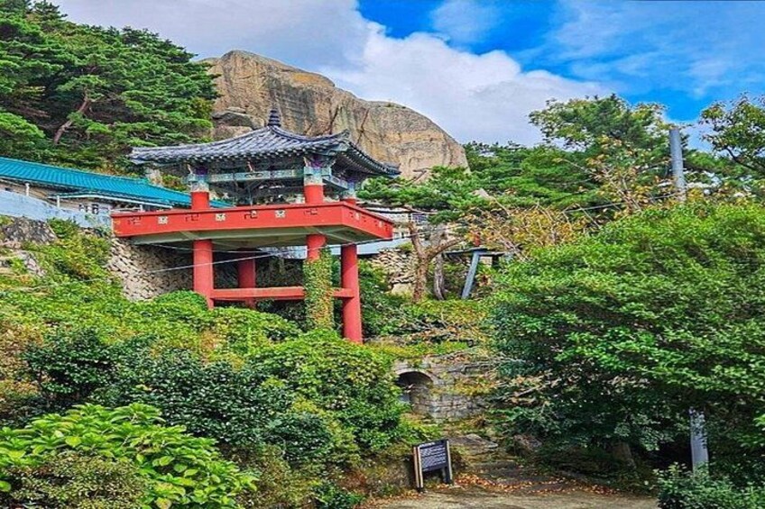 Een traditionele Koreaanse tempel met een rode poort, weelderige begroeiing en een rotsachtige berg op de achtergrond. 5